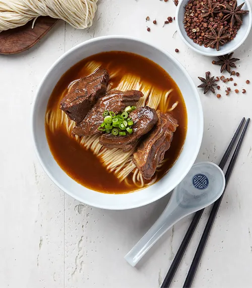 Top View of Braised Beef Noodle Soup in a bowl with Spoon for soup and Chopsticks for Noodles