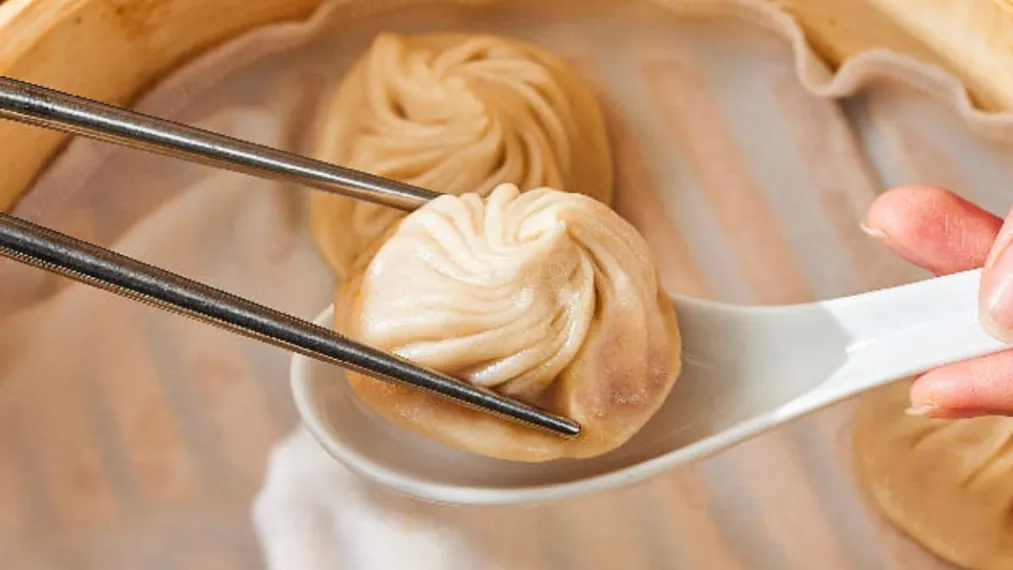 Kurobuta Pork Xiao Long Bao placed ni spoon held with chopstick