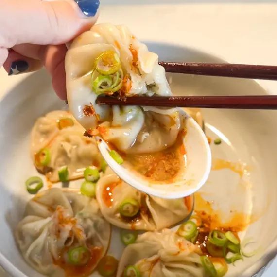a closeup of juice dumpling soup is in the spoon and dumpling is held by chopstick
